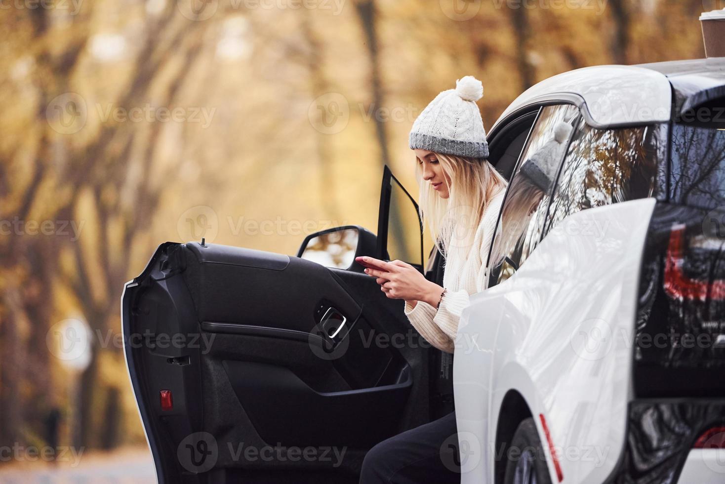 usando smartphones. menina tem viagem de outono de carro. automóvel novo e moderno na floresta foto