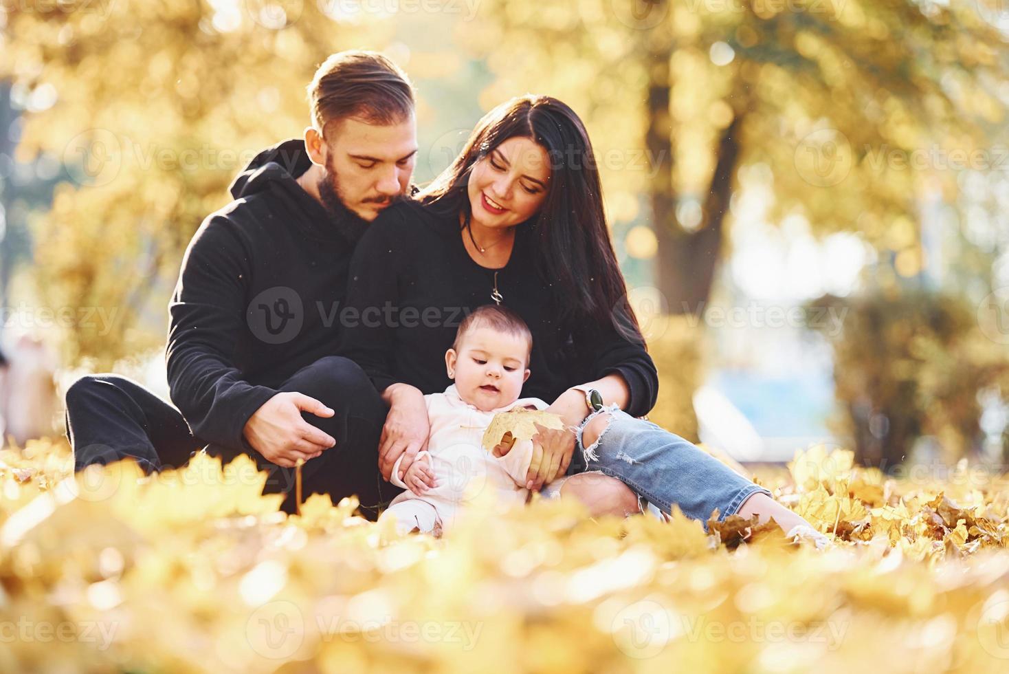 família alegre senta-se no chão e se diverte junto com seu filho no belo parque de outono foto