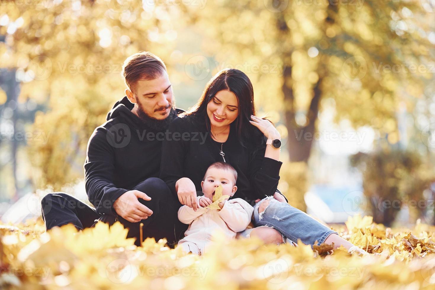 família alegre senta-se no chão e se diverte junto com seu filho no belo parque de outono foto