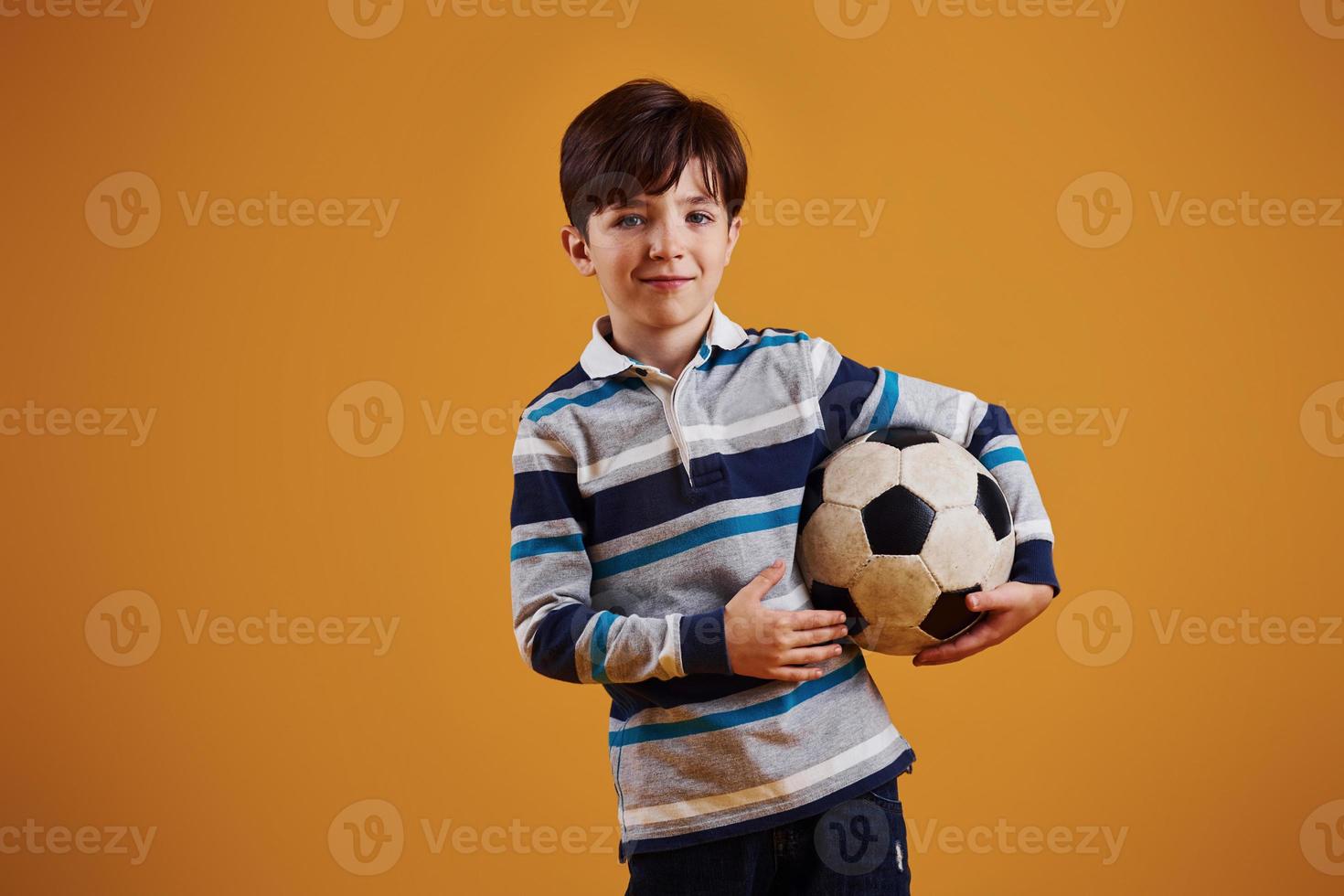 retrato de jovem jogador de futebol com bola. fica contra um fundo amarelo foto