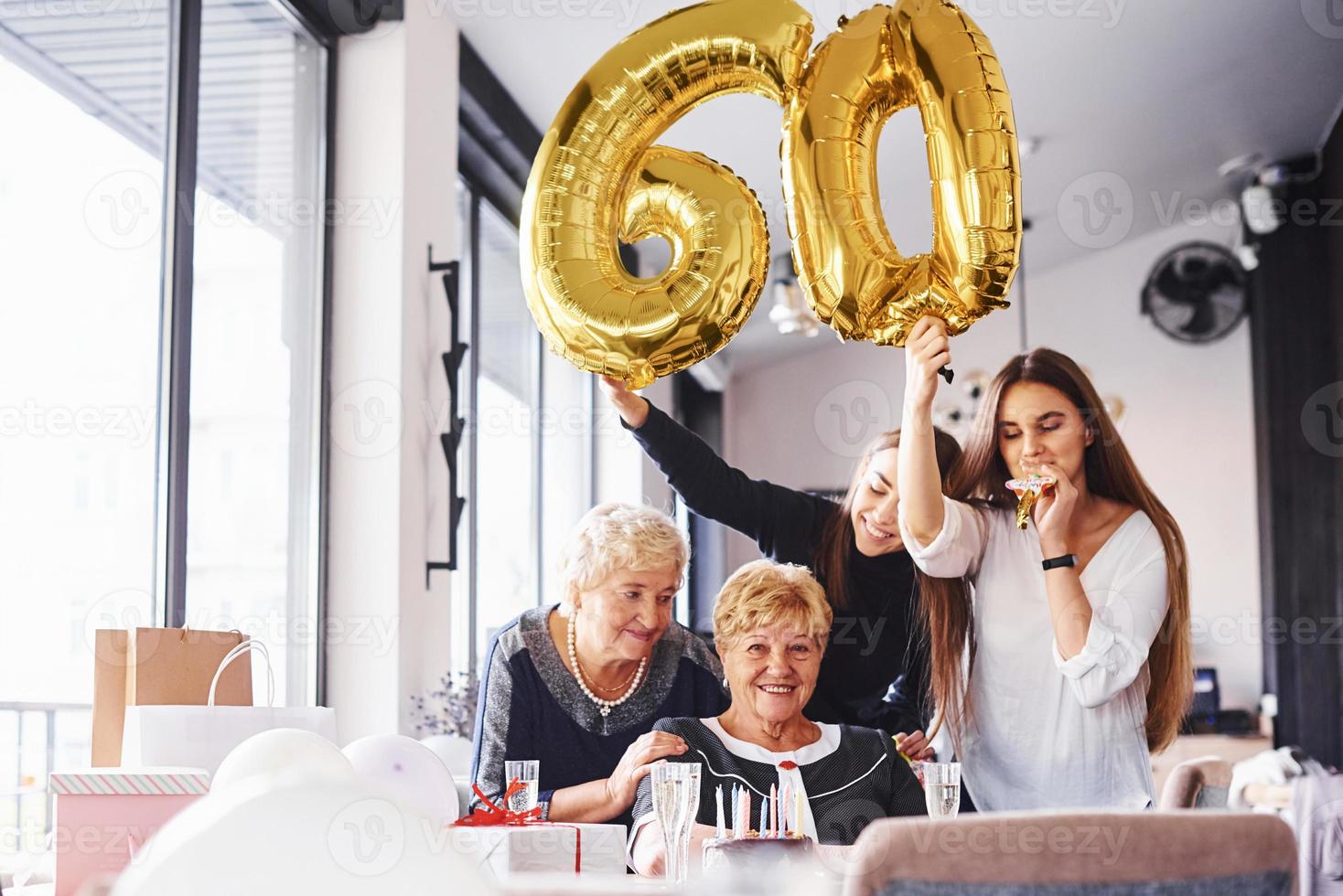 balões com o número 60. mulher sênior com família e amigos comemorando um aniversário dentro de casa foto