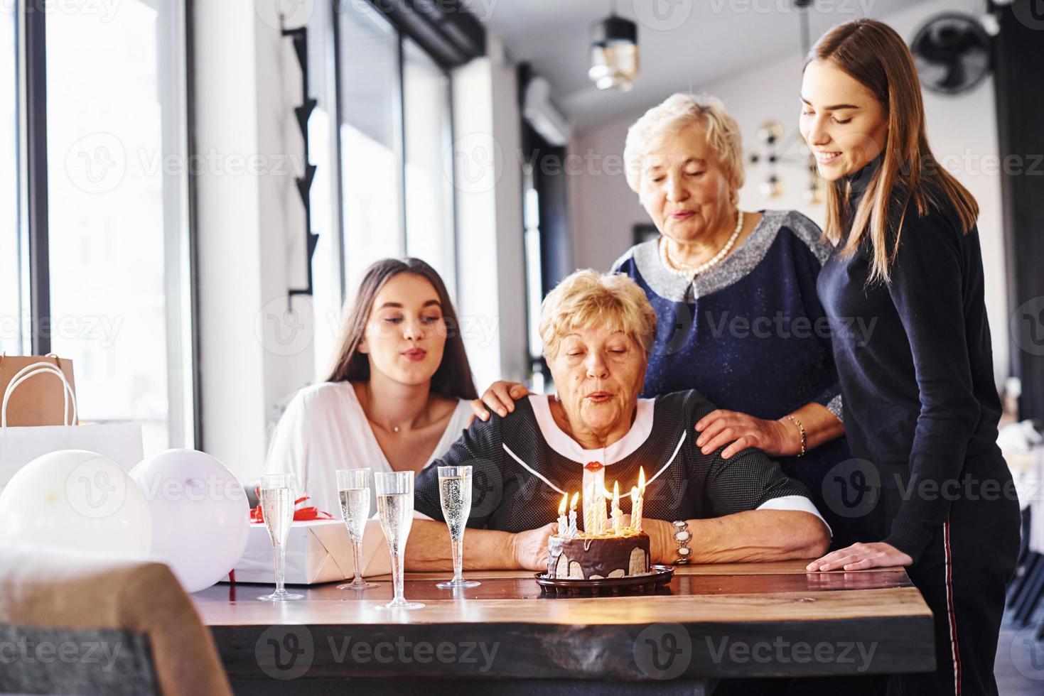 soprando as velas. mulher sênior com família e amigos comemorando um aniversário dentro de casa foto