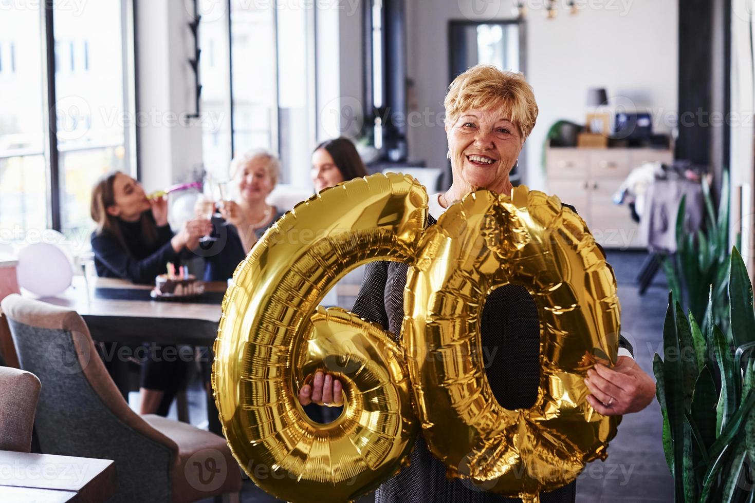 com balões de número 60 nas mãos. mulher sênior com família e amigos comemorando um aniversário dentro de casa foto