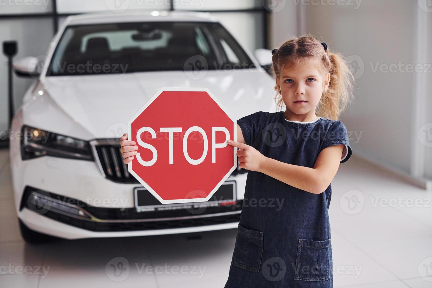 retrato de uma menina bonitinha que segura sinal de estrada nas mãos no salão do automóvel foto