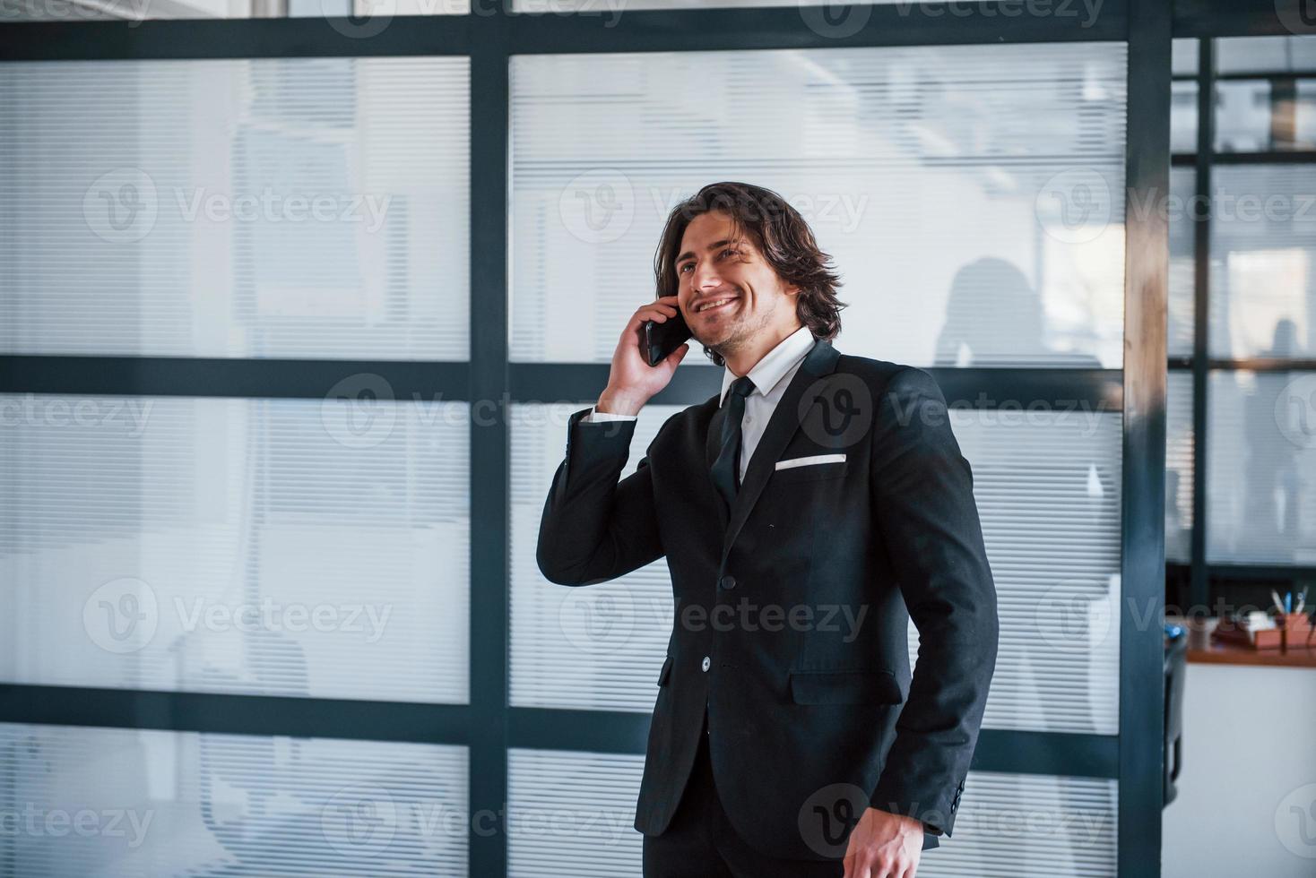 falando ao telefone no escritório. retrato do jovem empresário bonito de terno preto e gravata foto