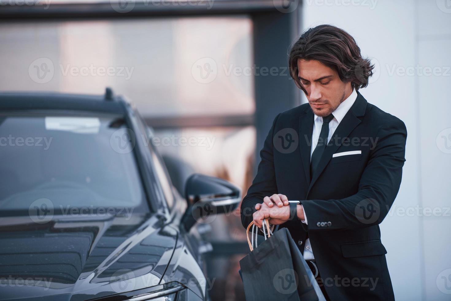 retrato de um jovem empresário bonito de terno preto e gravata ao ar livre perto de carro moderno foto