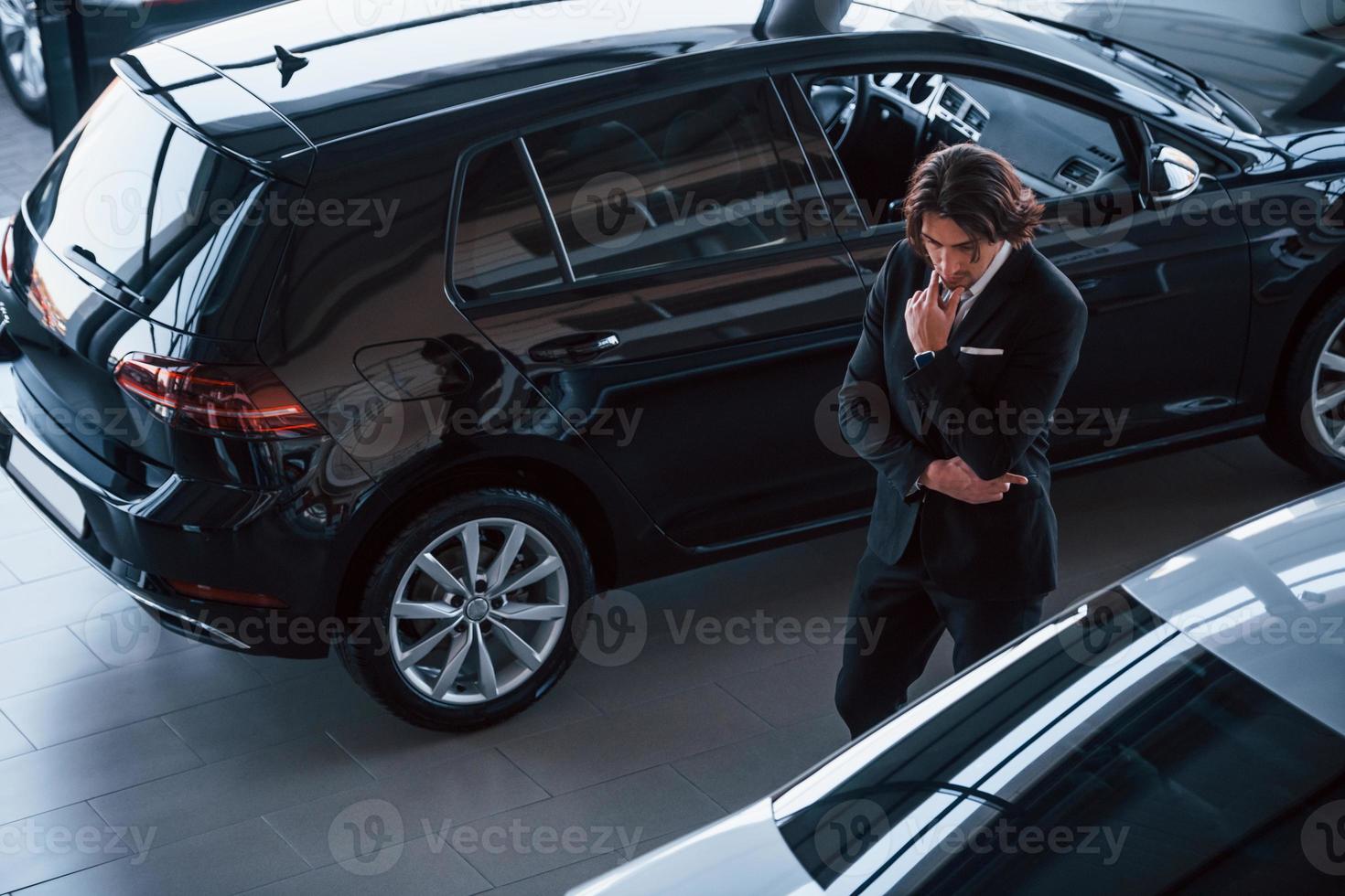 retrato de um jovem empresário bonito de terno preto e gravata dentro de casa perto de carro moderno foto