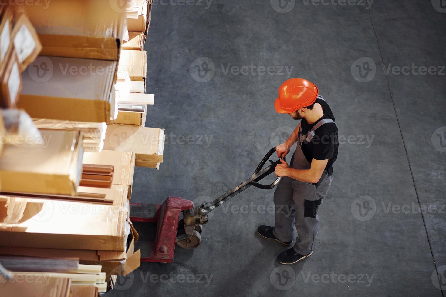 vista superior do jovem trabalhador de uniforme que está no armazém empurrando paleteira foto