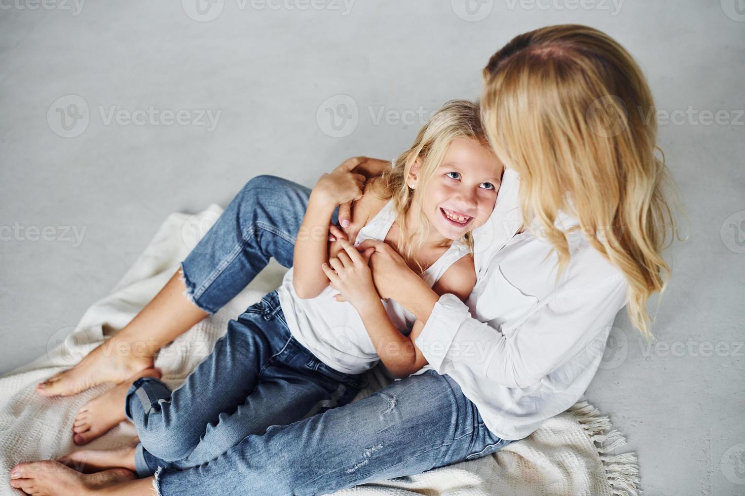 mãe com a filha está no chão no estúdio com fundo branco foto