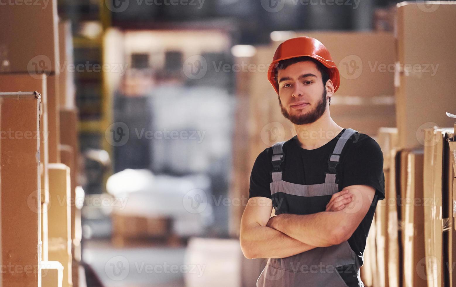retrato do jovem trabalhador de armazenamento no armazém de uniforme e capacete foto