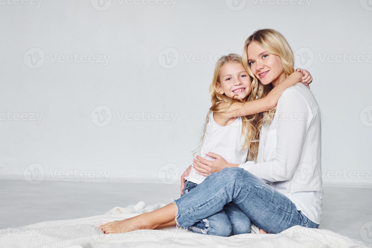 mãe com a filha está no chão no estúdio com fundo branco foto