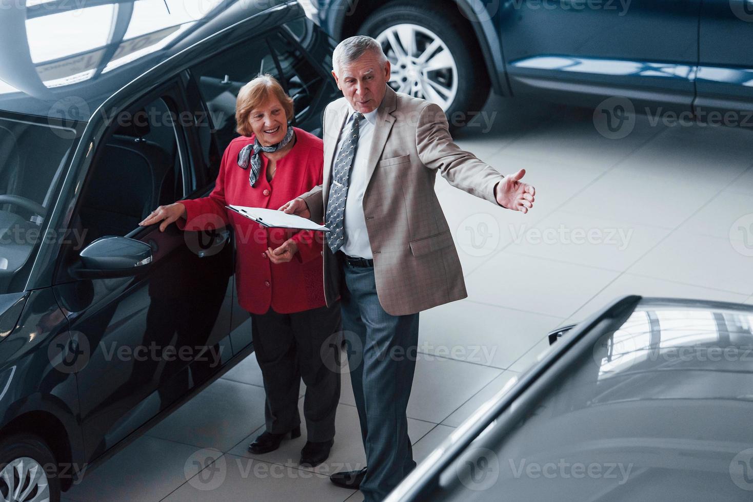 velho com roupa formal com o bloco de notas apoiando a mulher na escolha do automóvel foto