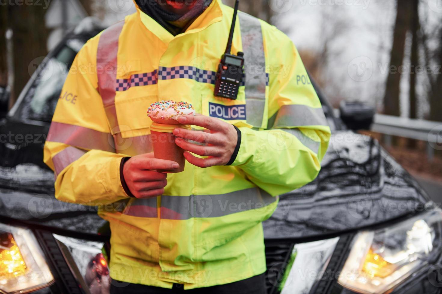 policial masculino de uniforme verde fazendo uma pausa com rosquinha na estrada foto