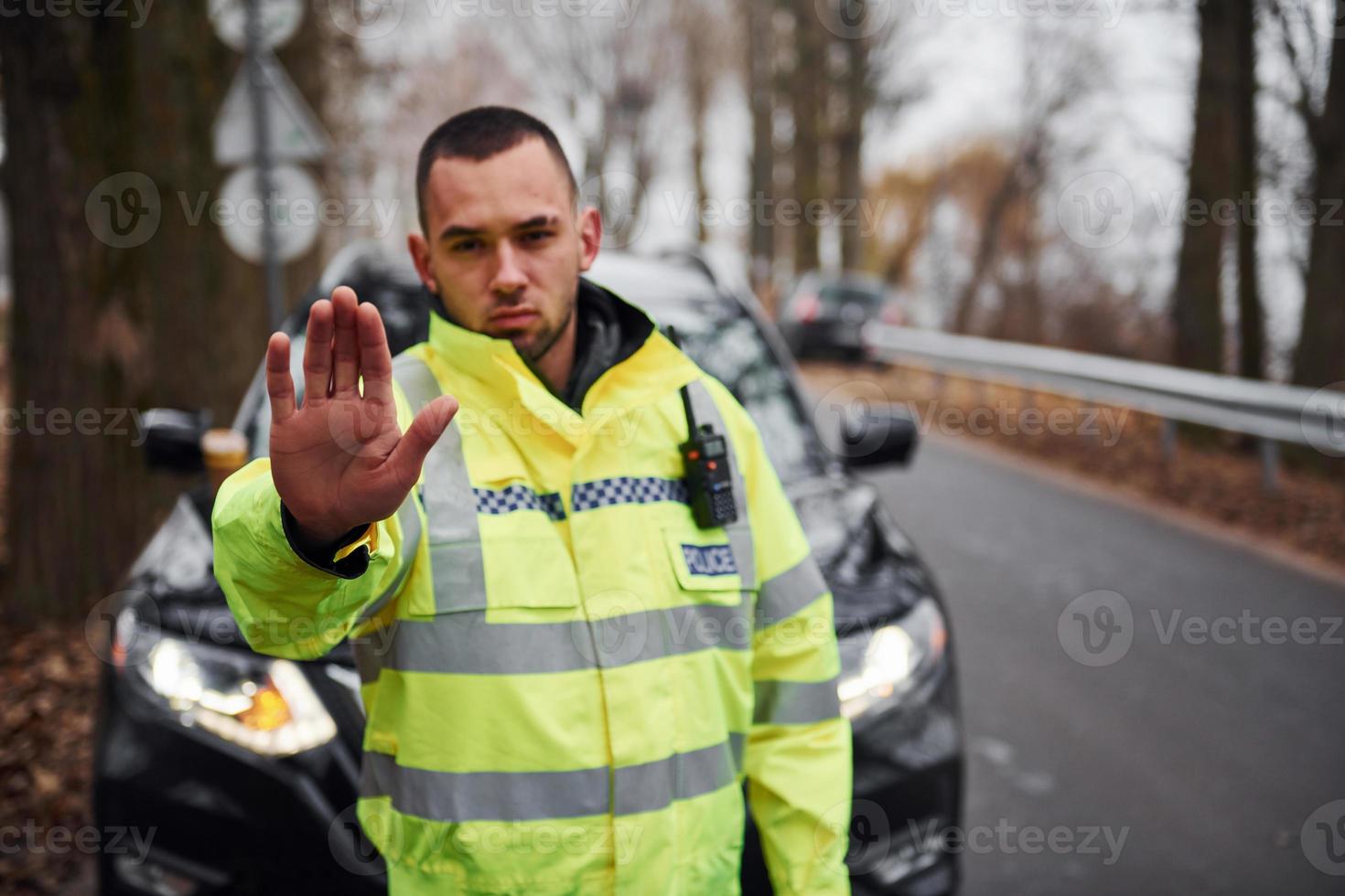 policial masculino em uniforme verde mostrando gesto de parada perto do veículo foto