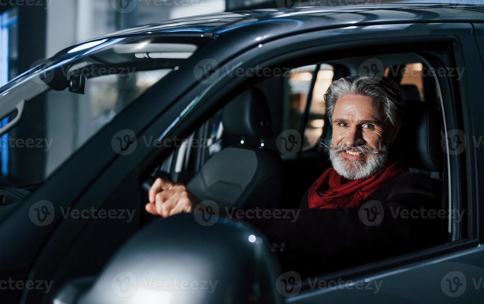 feliz elegante homem sênior com cabelos grisalhos e bigode está no carro moderno foto
