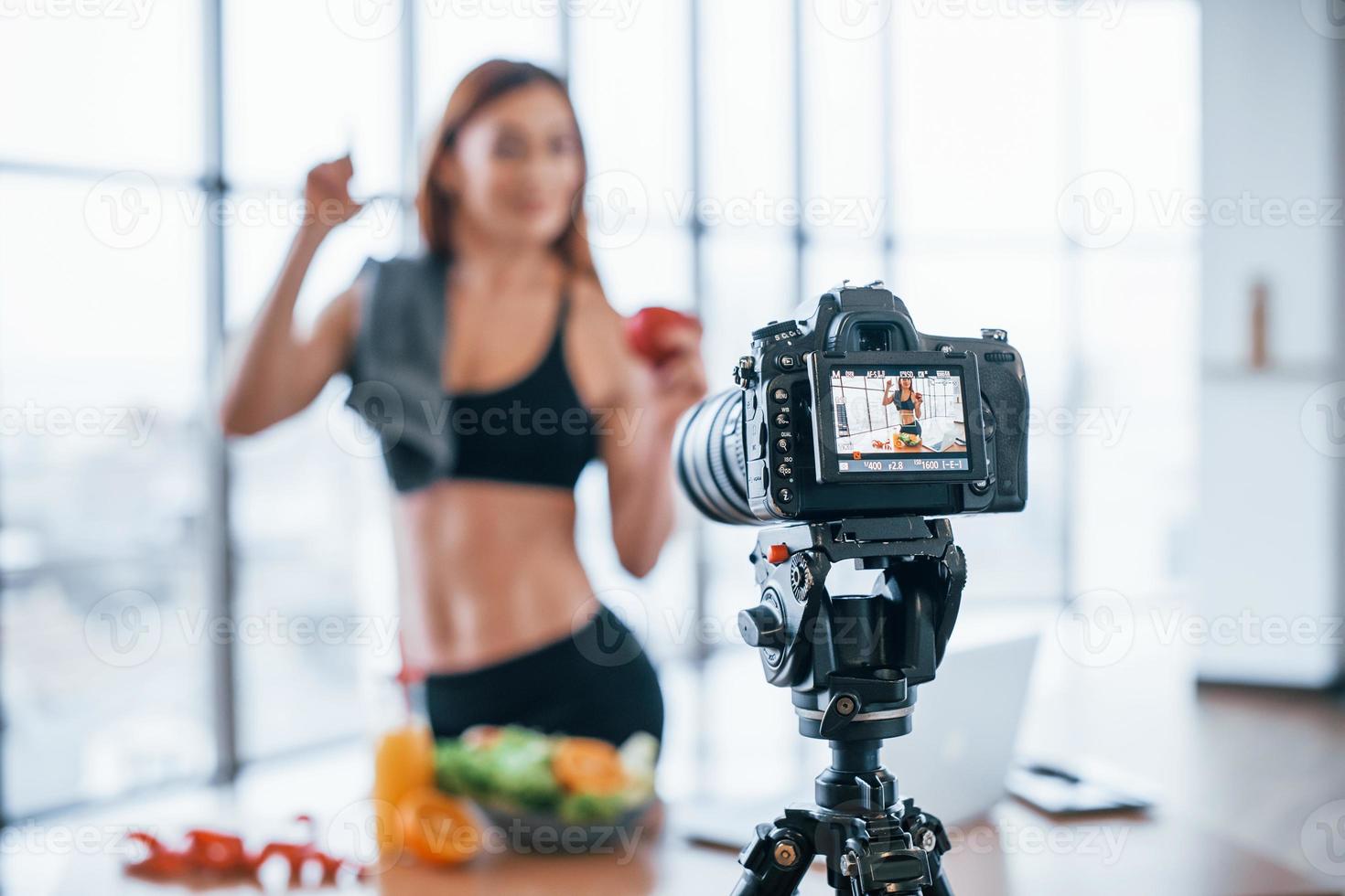 vlogger feminina com corpo esportivo em pé dentro de casa perto da mesa com comida saudável foto