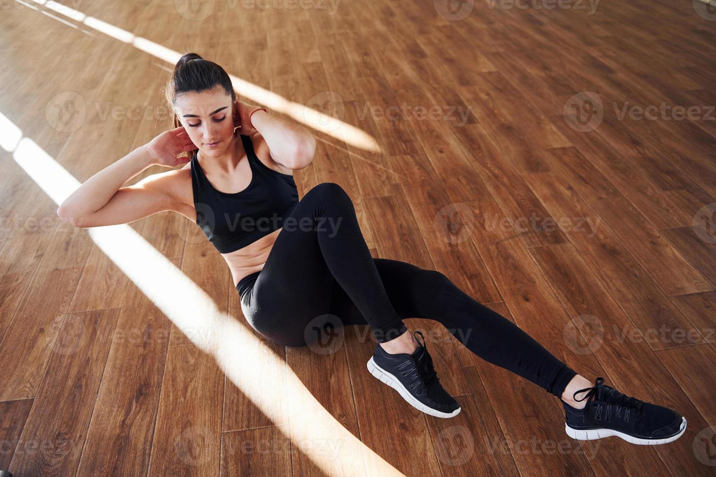 no chão iluminado por feixes de luz. jovem mulher desportiva em roupas esportivas fazendo fitness no ginásio foto