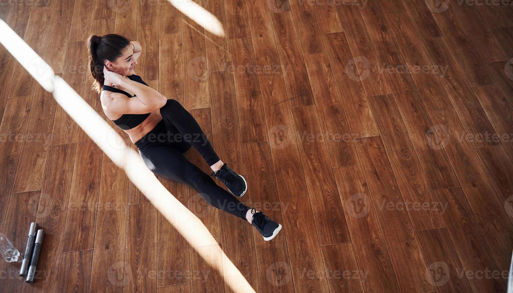 no chão iluminado por feixes de luz. jovem mulher desportiva em roupas esportivas fazendo fitness no ginásio foto