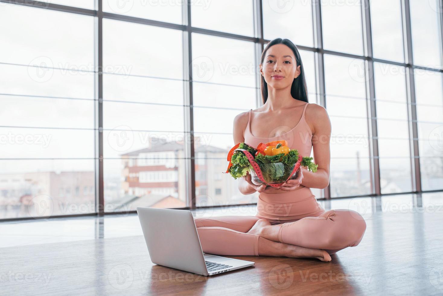 mulher esportiva sentada na mesa com laptop e comida saudável foto