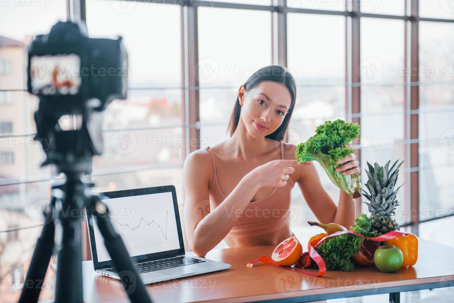 jovem vlogger fitness fazendo vídeo dentro de casa sentado perto da mesa com comida saudável foto