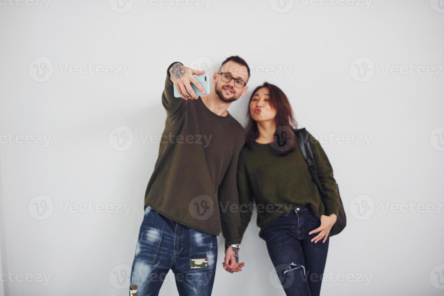 alegre casal multiétnico em roupas casuais fazendo selfie dentro de casa no estúdio contra fundo branco foto