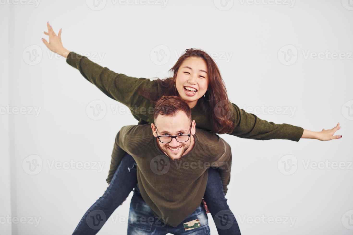 feliz casal multiétnico em roupas casuais se divertem juntos dentro de casa no estúdio. cara caucasiano com namorada asiática foto