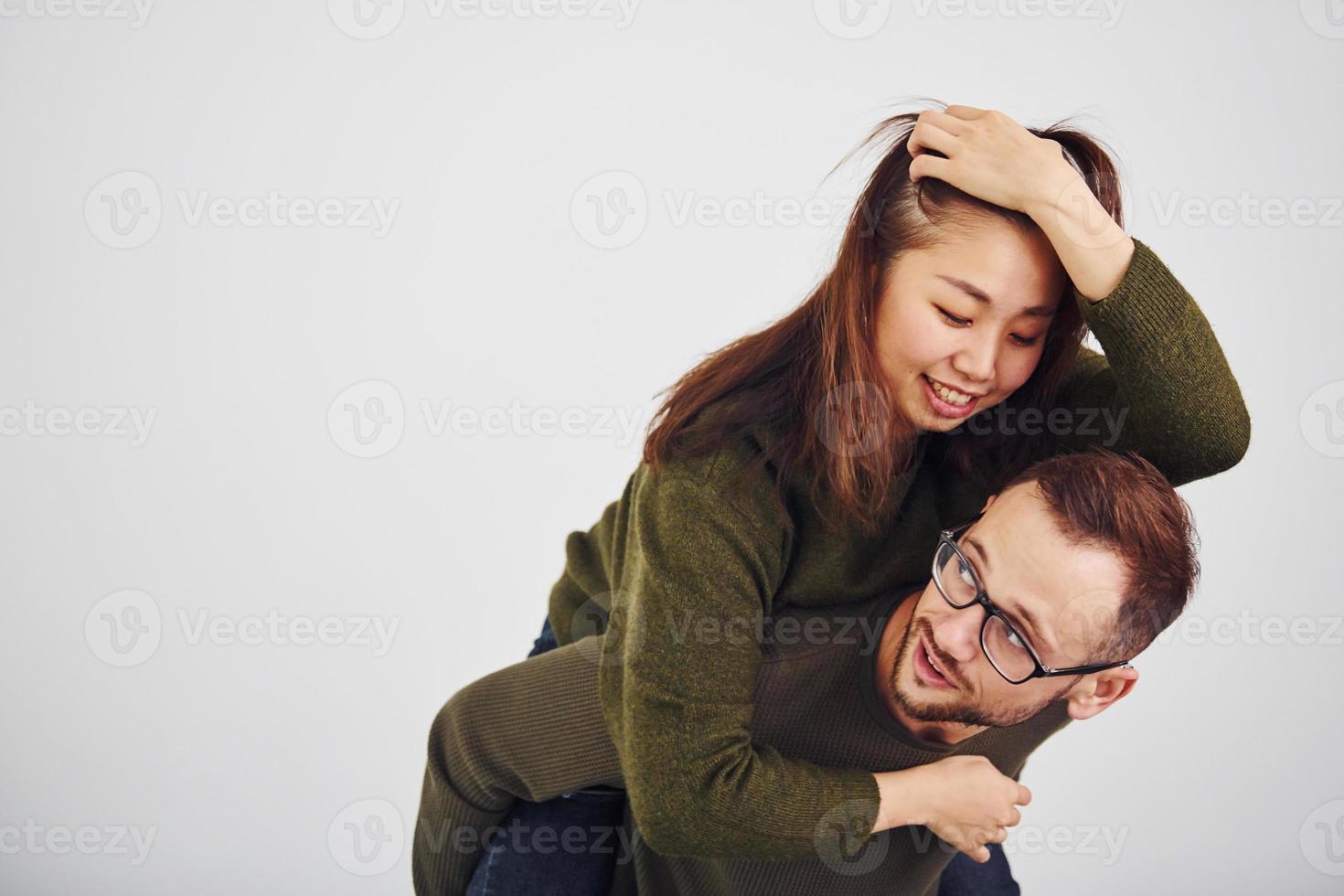 feliz casal multiétnico em roupas casuais se divertem juntos dentro de casa no estúdio. cara caucasiano com namorada asiática foto