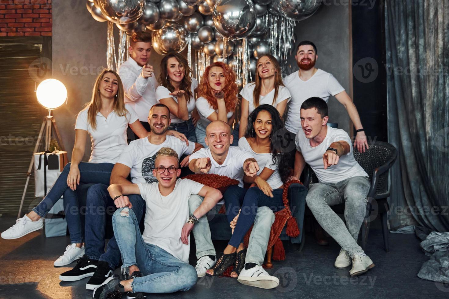 jovens positivos sentados e comemorando o ano novo na sala decorada de natal com balões juntos foto