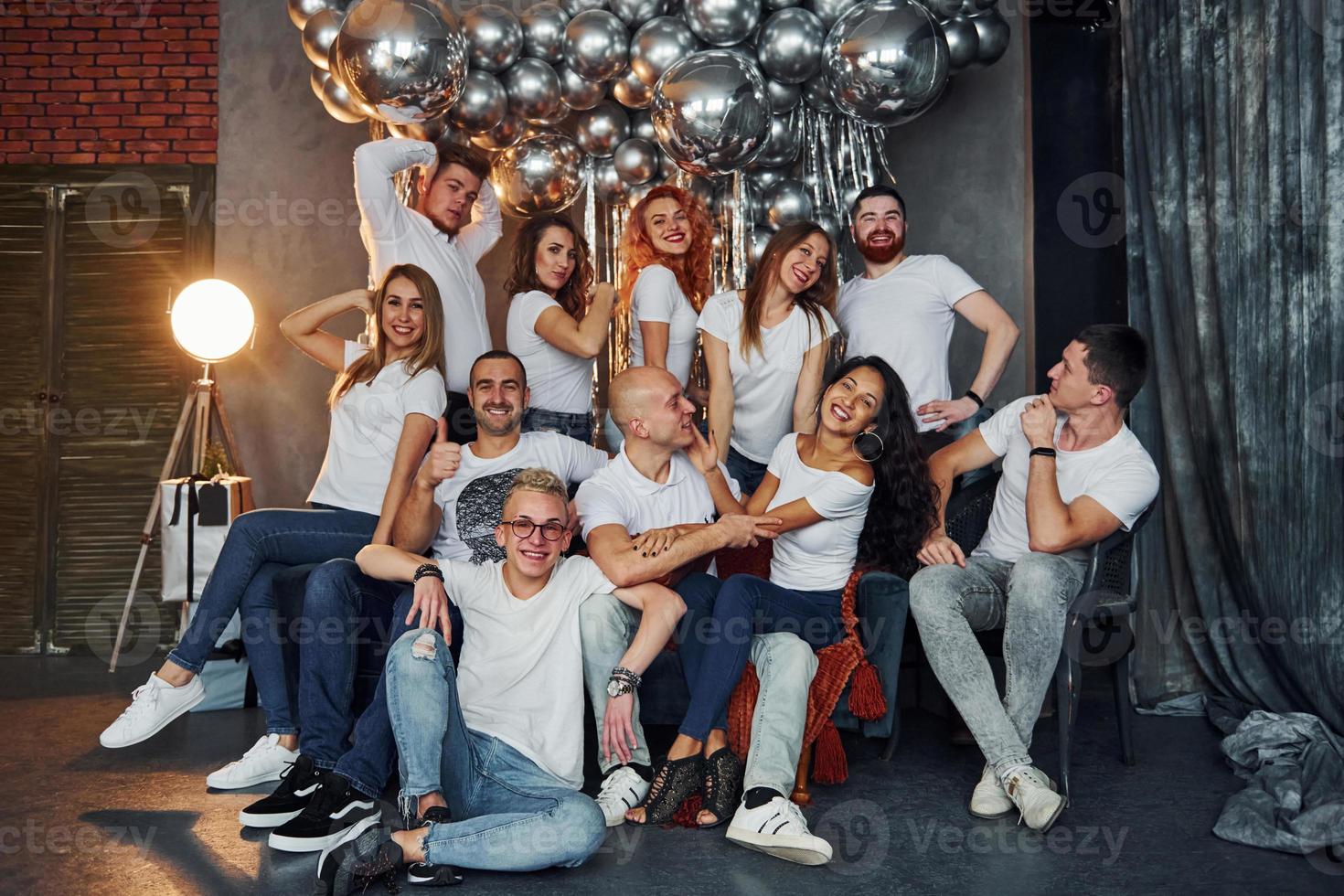 jovens positivos sentados e comemorando o ano novo na sala decorada de natal com balões juntos foto