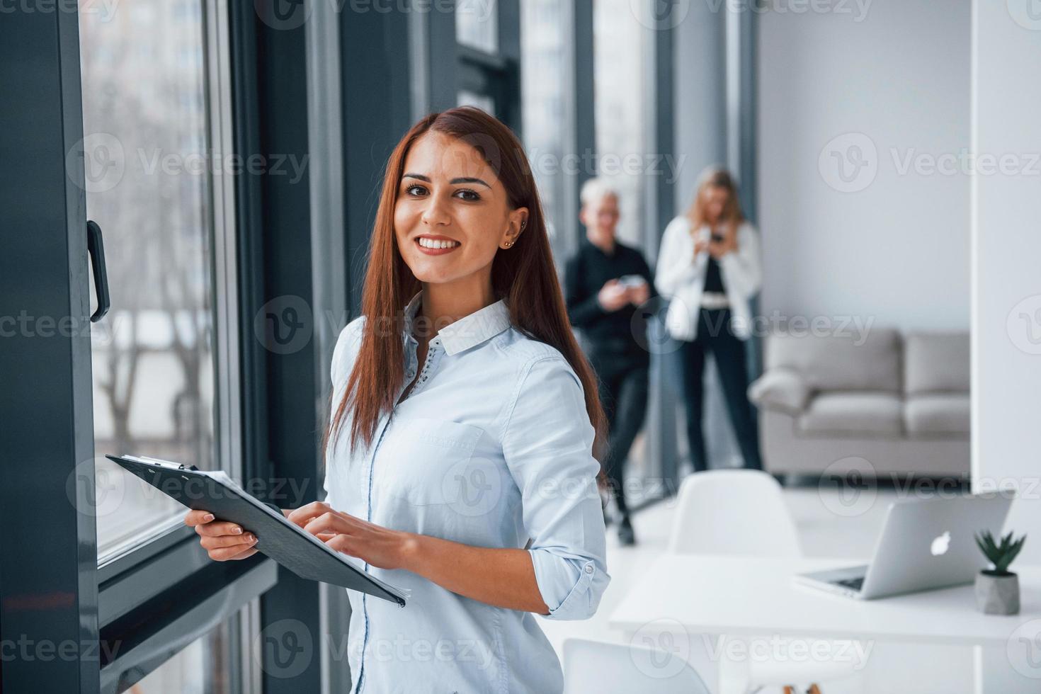 retrato de mulher com bloco de notas que está na frente do grupo de jovens equipe de sucesso que trabalham e se comunicam juntos dentro de casa no escritório foto