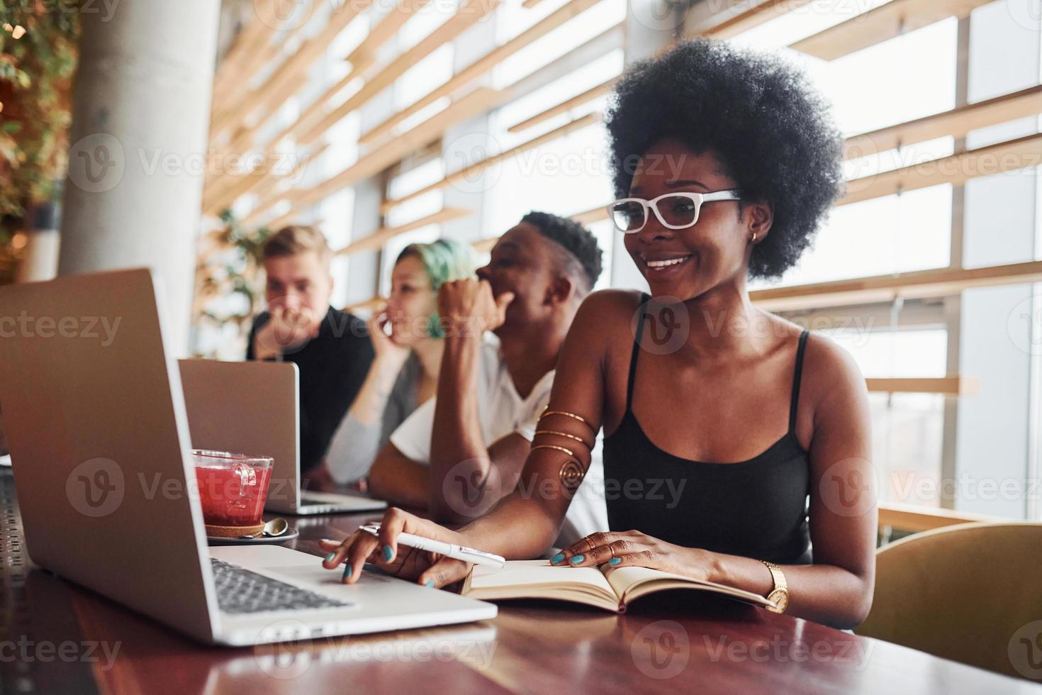 mulher negra sentada na frente de um grupo de pessoas multiétnicas com uma garota alternativa de cabelo verde está trabalhando junto à mesa dentro de casa foto