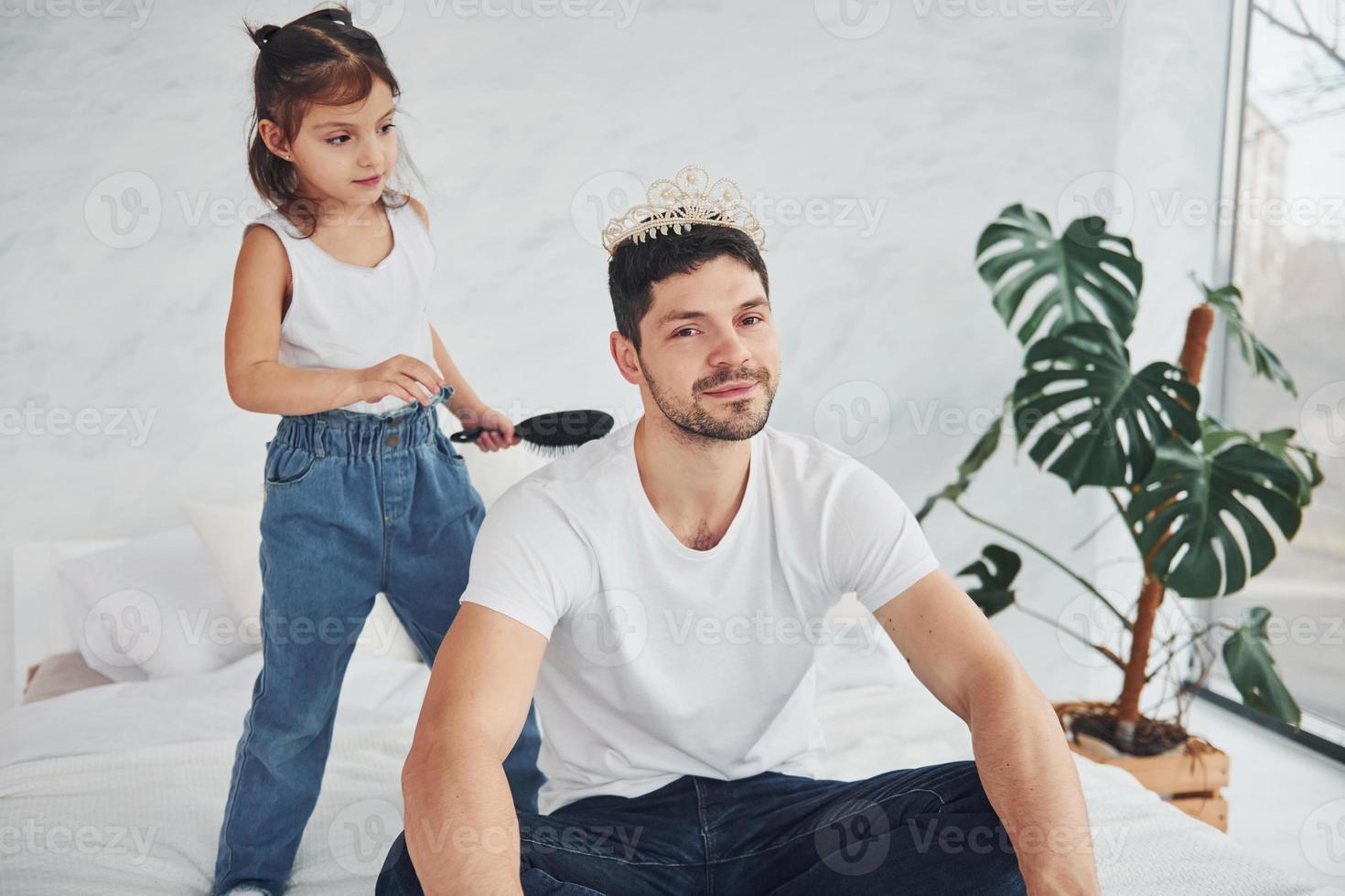 menina usando coroa na cabeça do pai. se divertindo em casa juntos foto