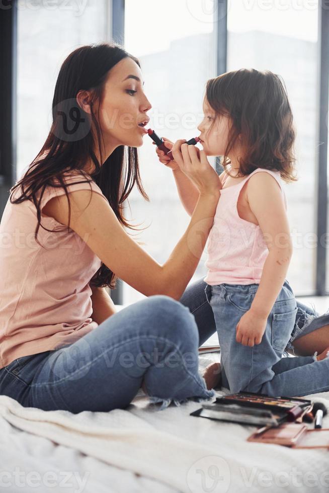 aprendendo a se maquiar. jovem mãe com a filha passando o fim de semana juntos no quarto foto