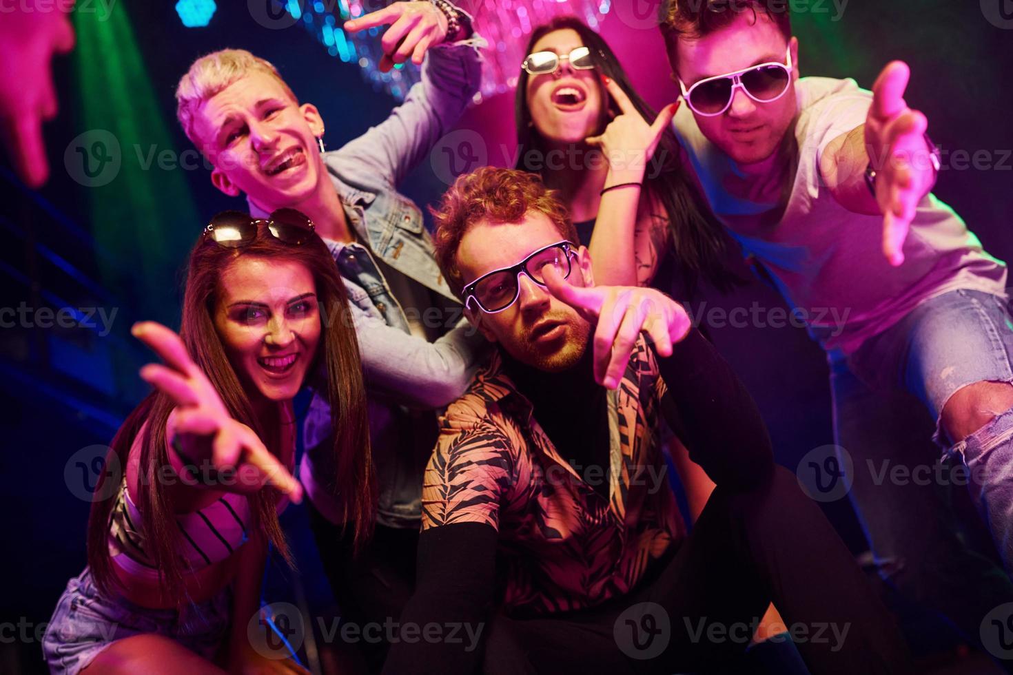 enlouquecendo e posando para a câmera juntos. os jovens estão se divertindo na boate com lasers coloridos foto