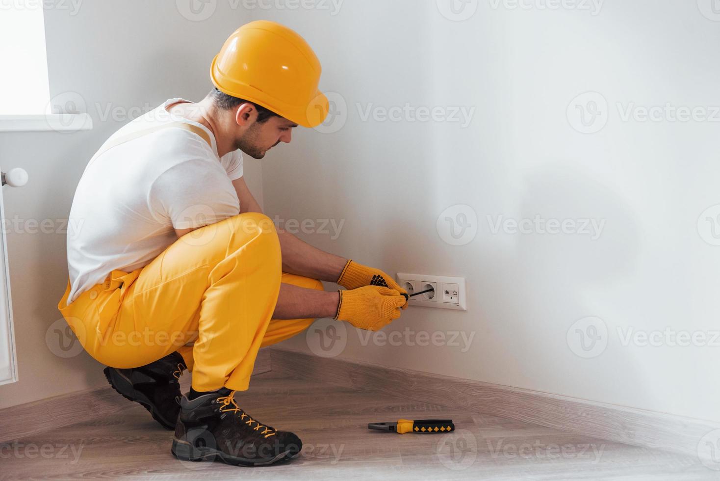 trabalhador braçal de uniforme amarelo trabalha com eletricidade e instala nova tomada. concepção de renovação de casa foto