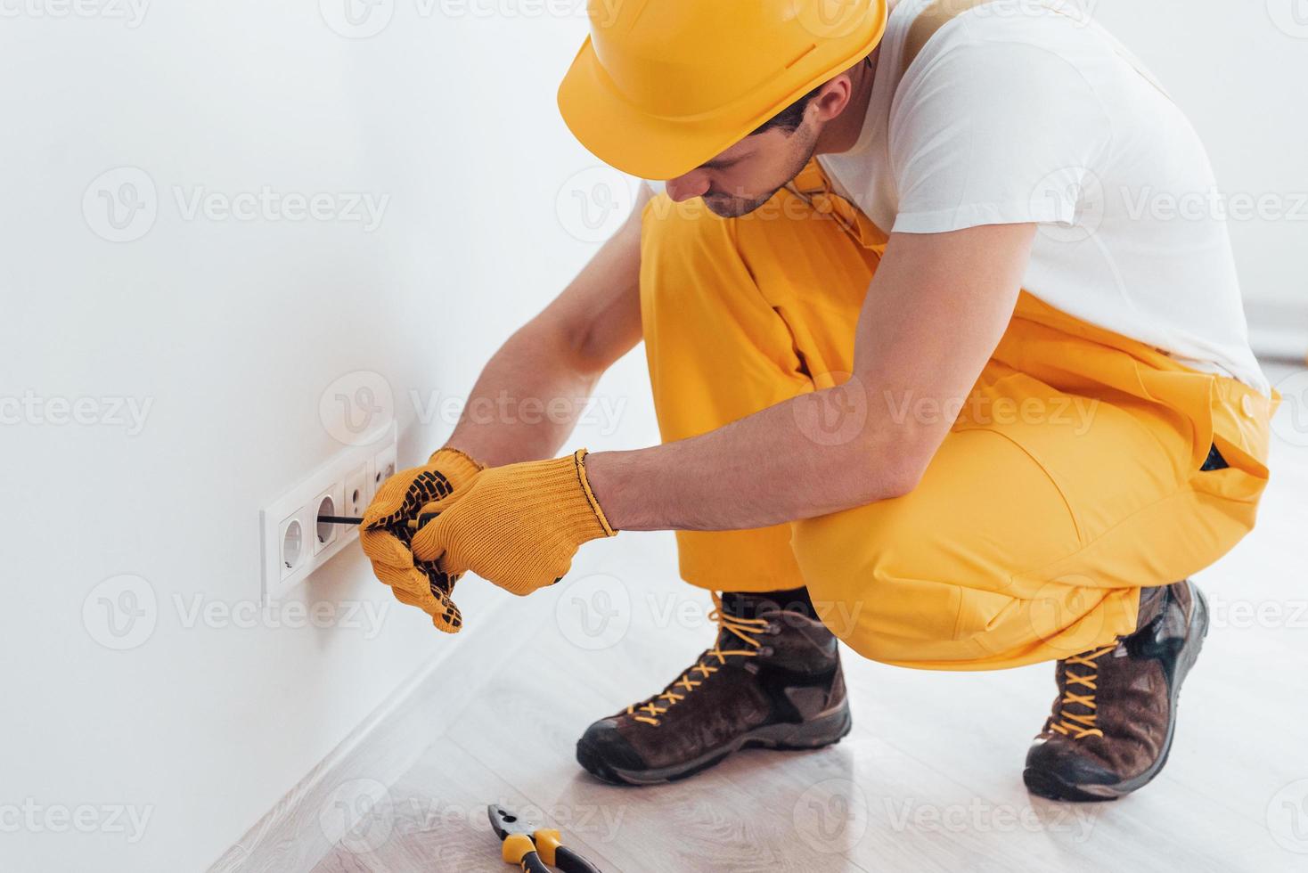 trabalhador braçal de uniforme amarelo trabalha com eletricidade e instala nova tomada. concepção de renovação de casa foto