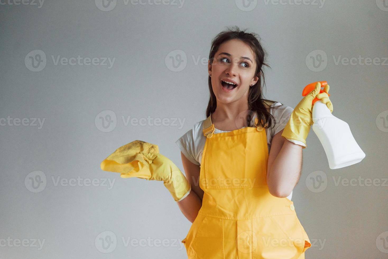 dona de casa em pé de uniforme amarelo com spray de limpeza para janelas dentro de casa. concepção de renovação de casa foto