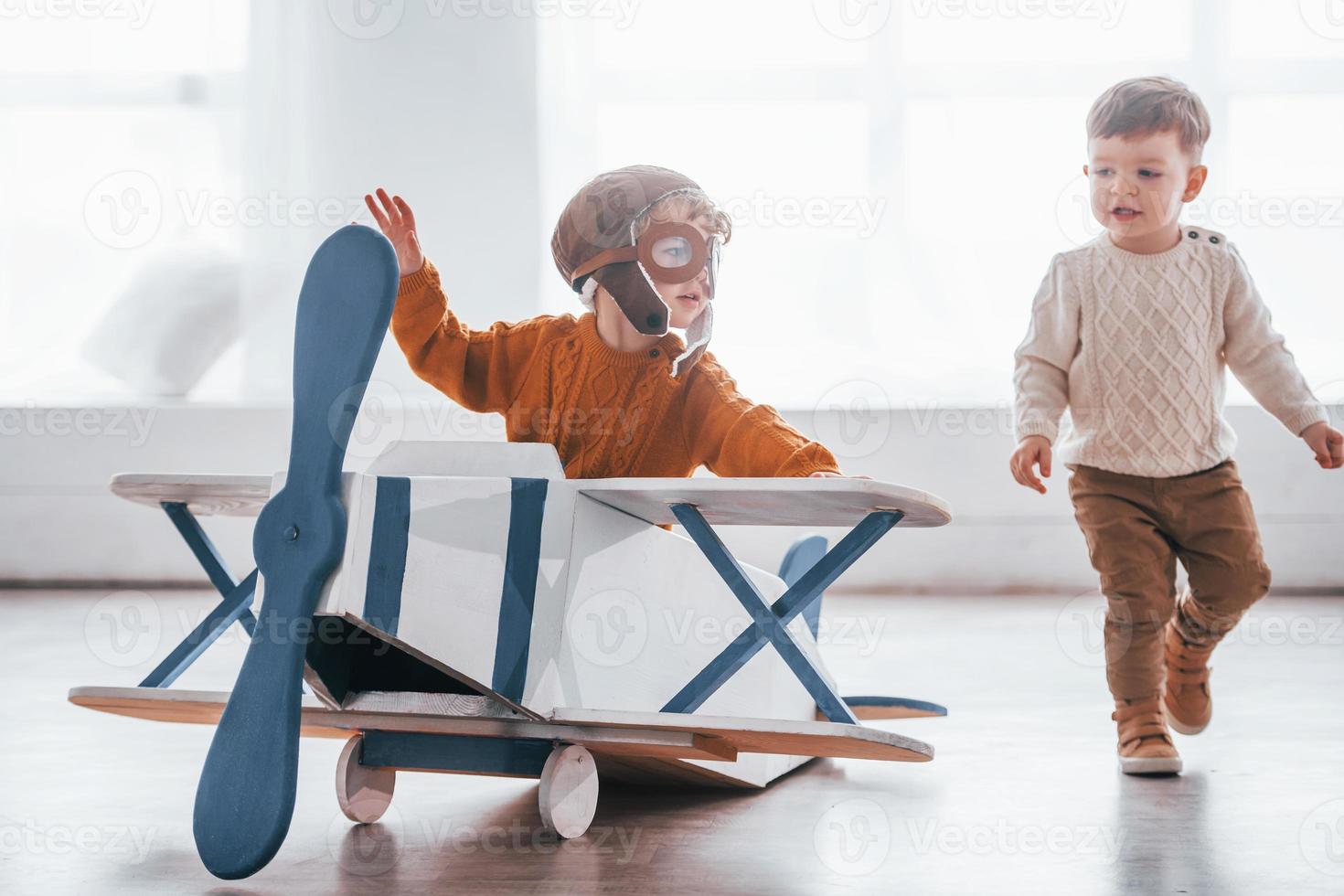 dois meninos em uniforme de piloto retrô se divertindo com avião de brinquedo dentro de casa foto