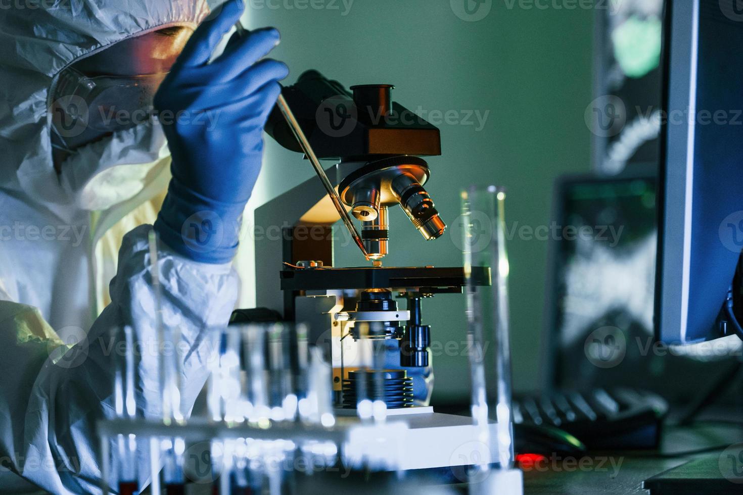 cientista em uniforme protetor branco trabalha com coronavírus e tubos de sangue em laboratório foto
