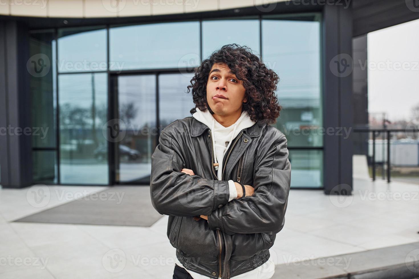 jovem bonito com cabelo preto encaracolado está na rua contra a construção foto