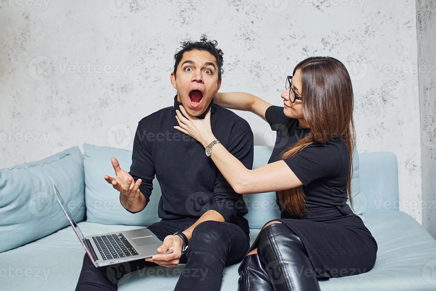 homem com cabelo cacheado e mulher que em roupas pretas sentadas com laptop dentro de casa e se divertem foto