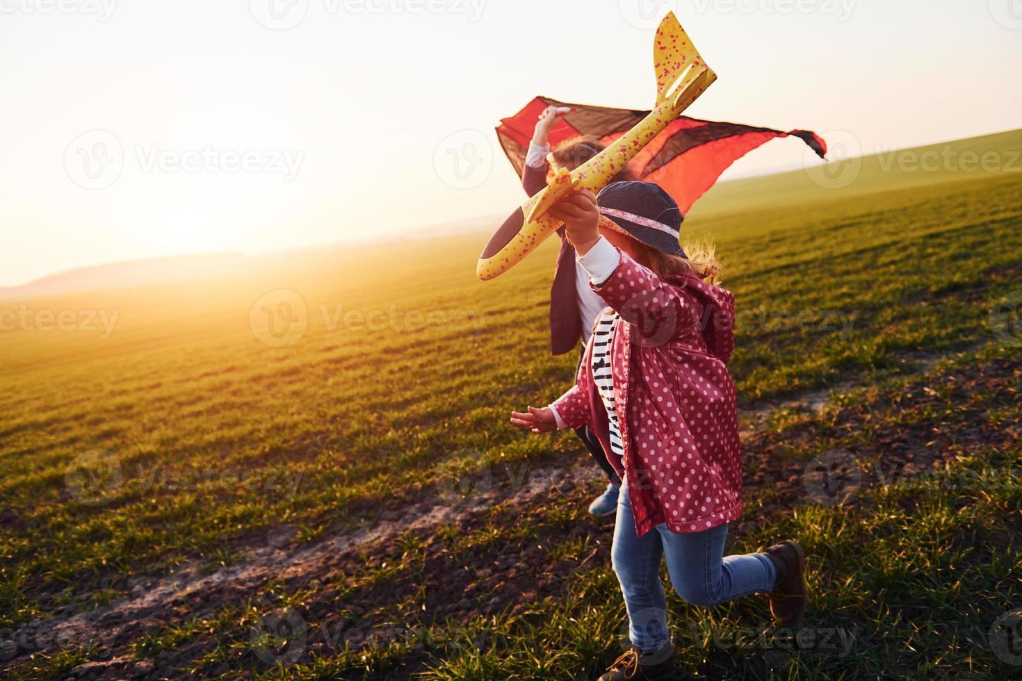 menina bonitinha corre com avião de brinquedo no belo campo durante o dia ensolarado foto