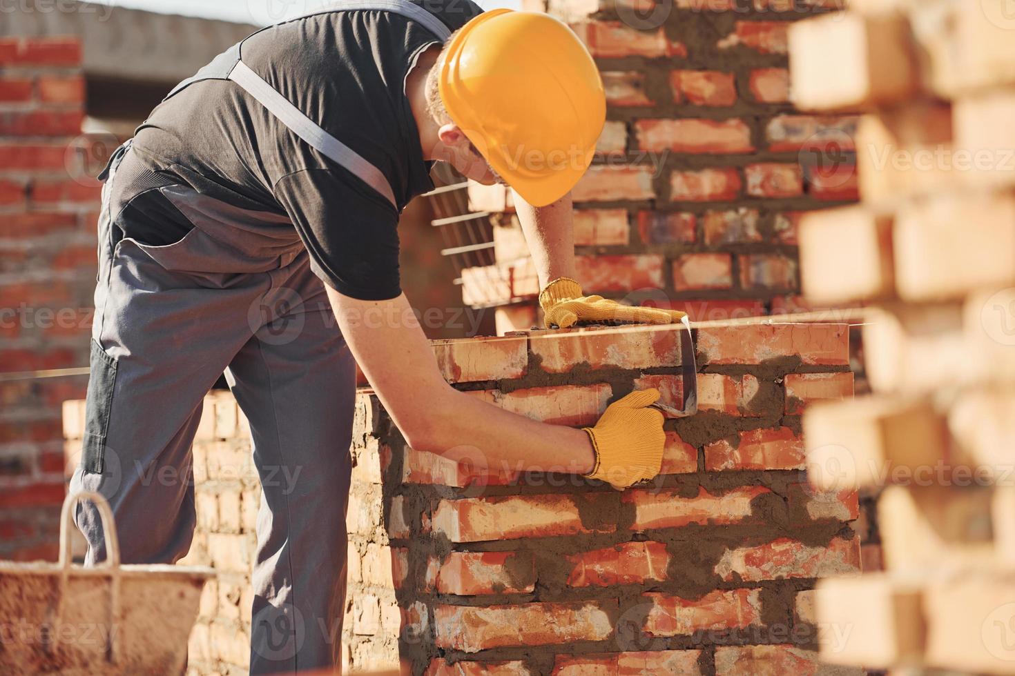 ocupado com a parede de tijolos. trabalhador da construção civil em equipamentos uniformes e de segurança tem trabalho na construção foto