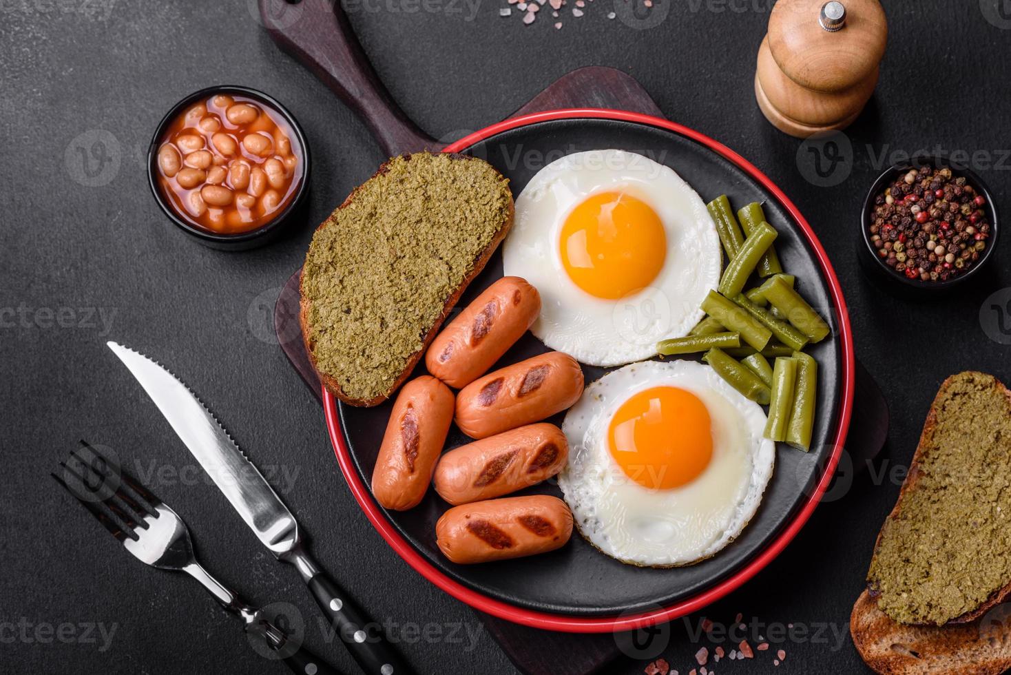 saboroso café da manhã inglês com ovos fritos, feijão, aspargos, salsichas com especiarias e ervas foto