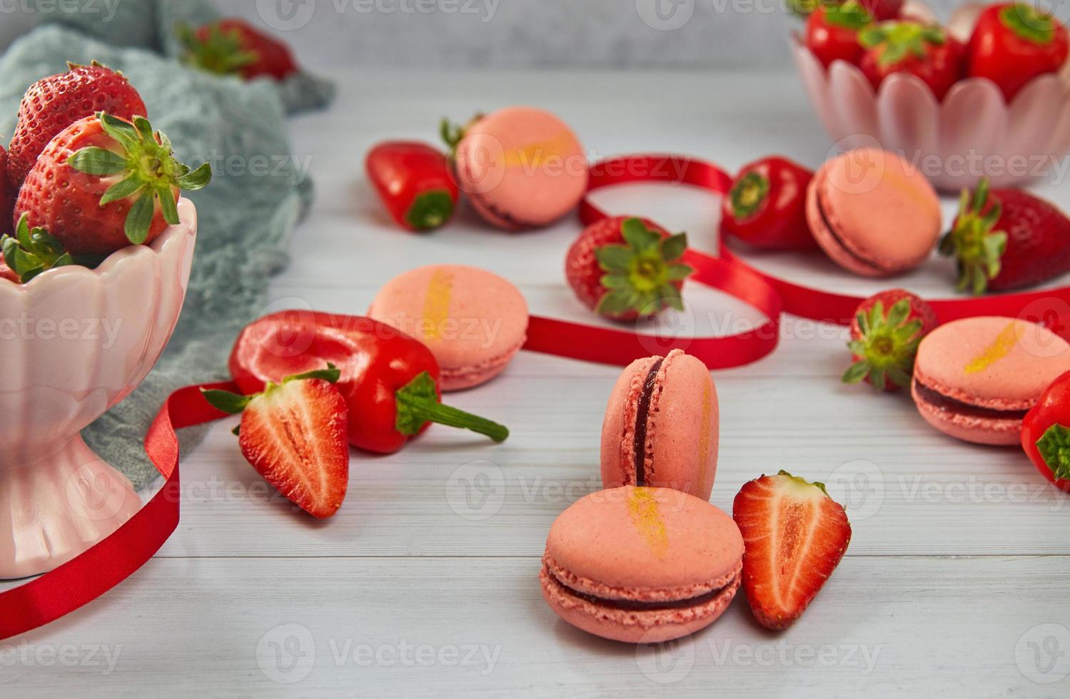 macarons de morango de cor rosa com morangos e pimentões na luz de fundo de madeira foto