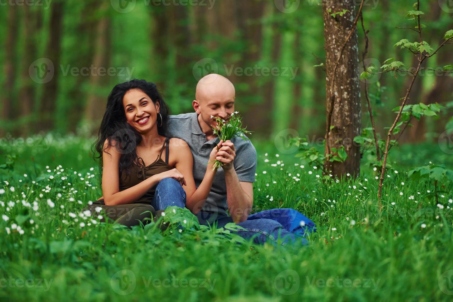 casal feliz sentado na grama juntos na floresta durante o dia foto