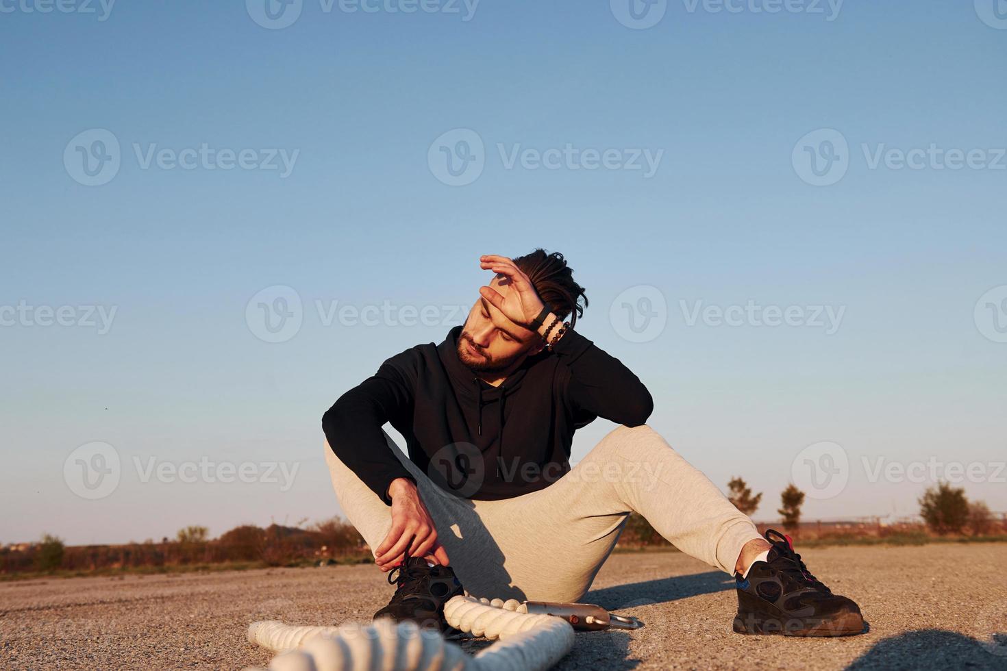 homem em roupas esportivas sentado na estrada ao entardecer com cordas e descansando foto