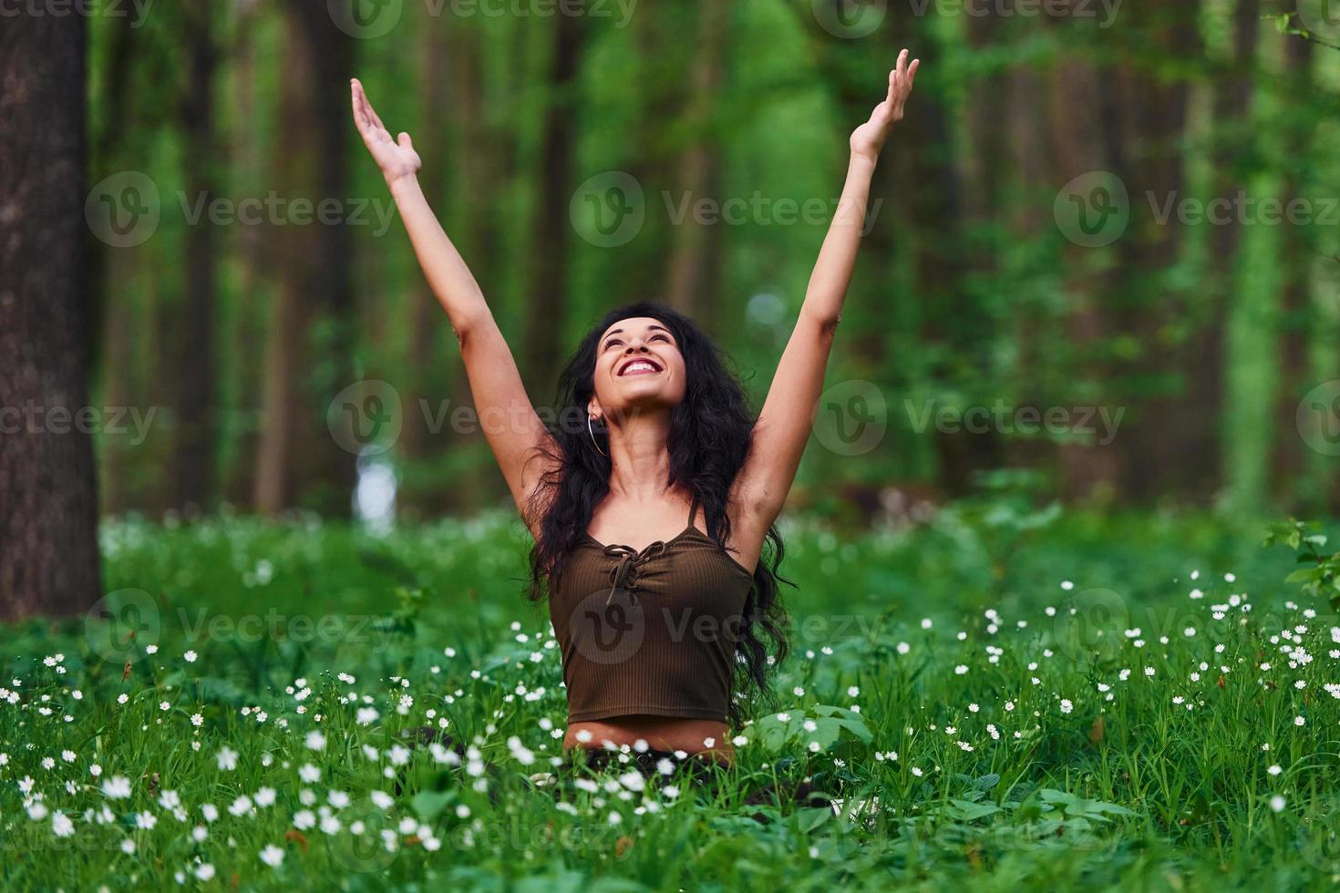 morena positiva em roupas casuais sentada na floresta durante o dia foto