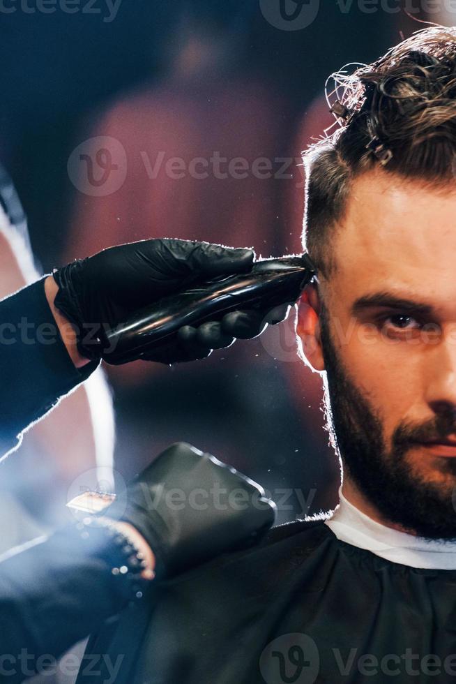 close-up vista do jovem barbudo que sentado e cortando o cabelo na barbearia foto