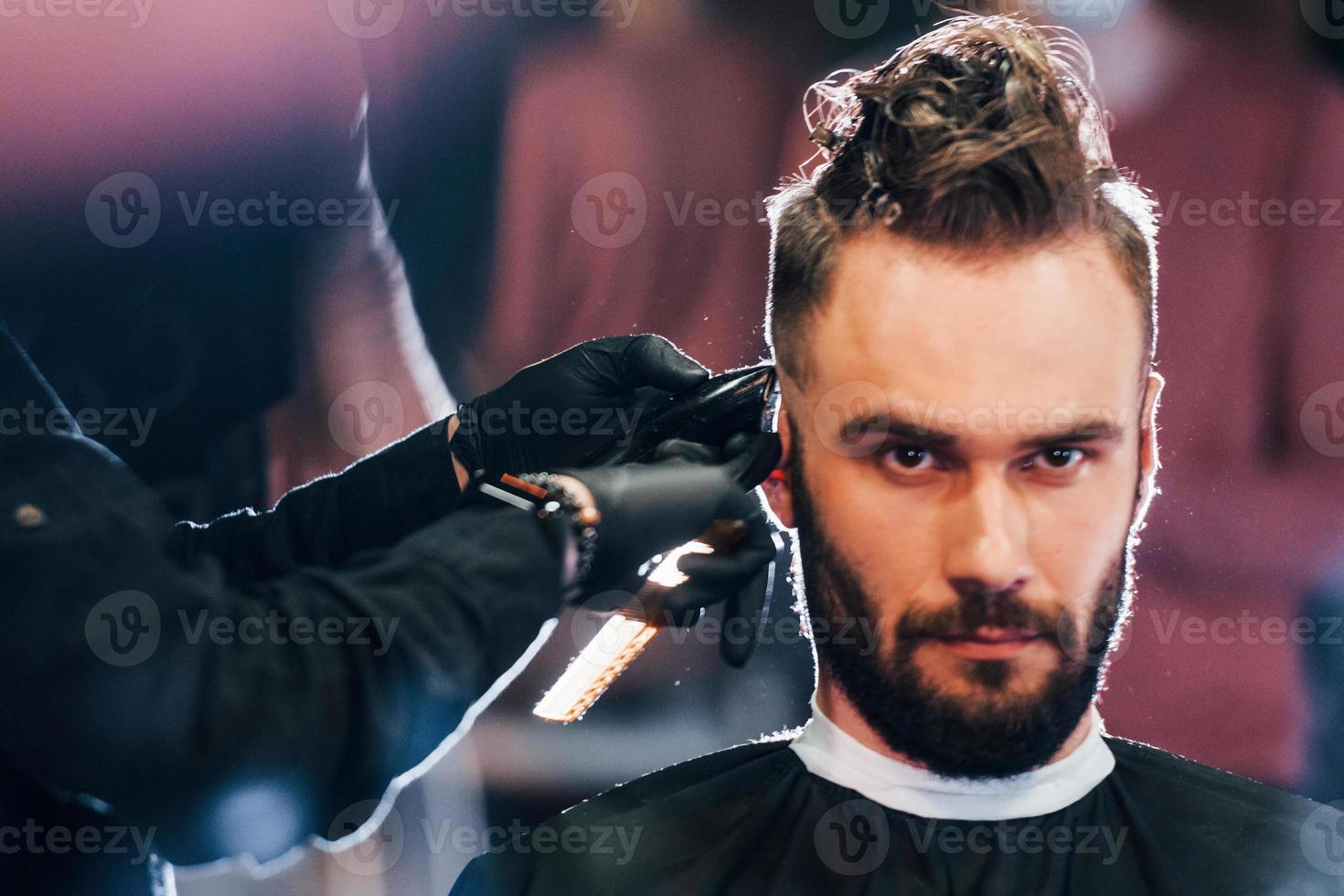 jovem barbudo sentado e cortando o cabelo na barbearia foto